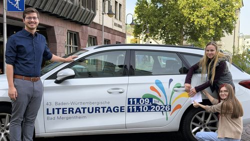 Bad Mergentheim im Literaturtage-Fieber: Lukas Wegner, Sachgebietsleiter Tourismus & Kultur, bedankt sich bei Sophia Leuchs (2. von rechts) und Jessica Ehrler fürs Bekleben der städtischen Fahrzeuge.